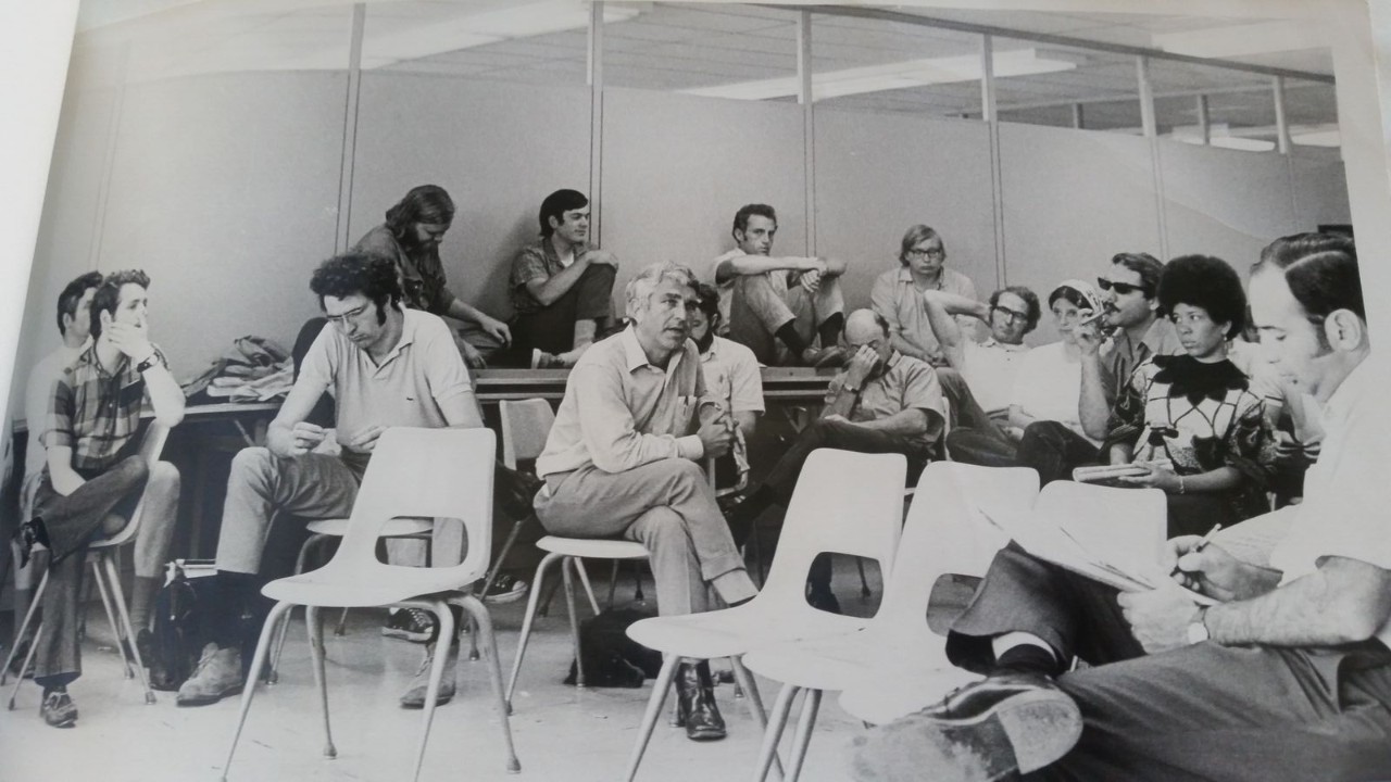 A man sits in a chair surrounded by listening students.