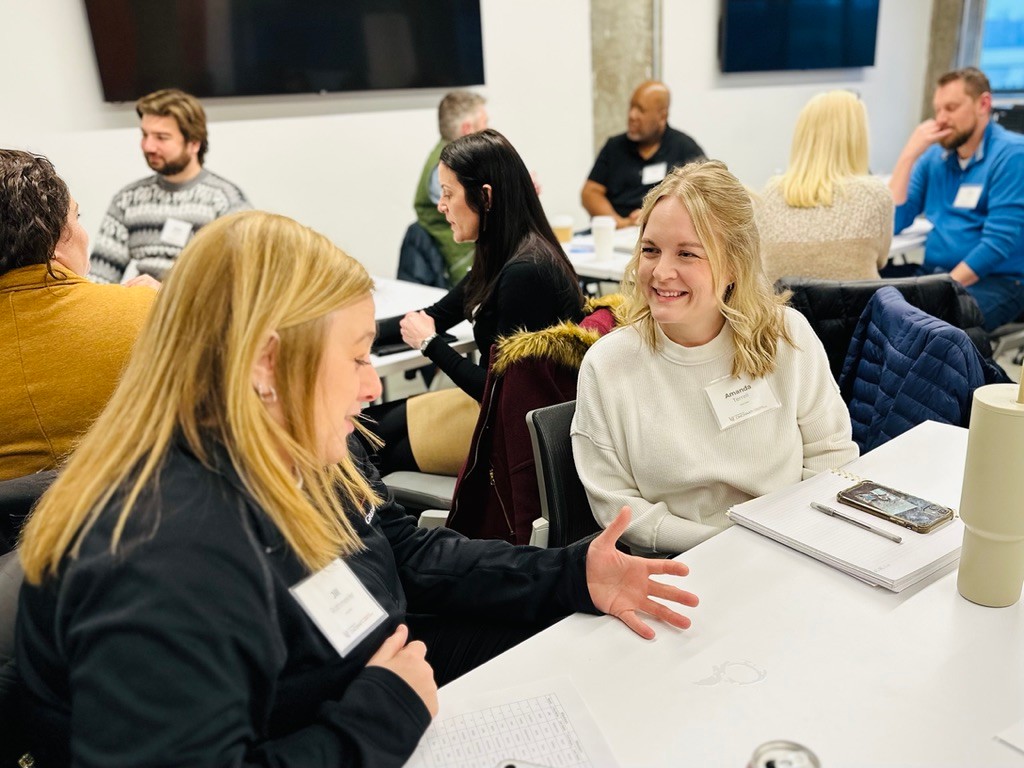 Two women speak to each other while sitting at a table.