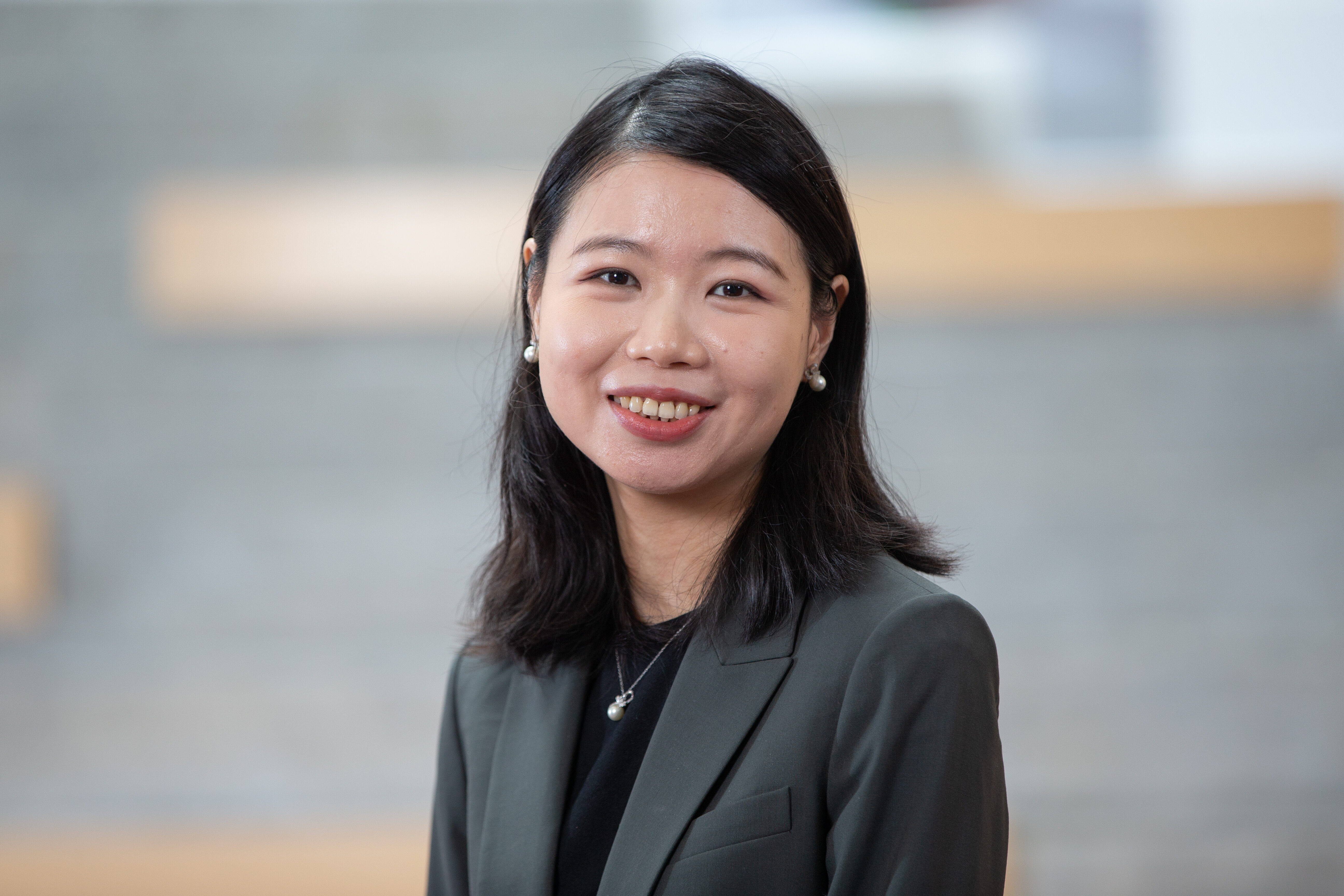 A woman in a dark gray jacket and black shirt smiles.