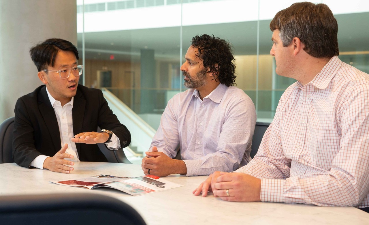 Thee men sit at a table in professional dress and talk about research.