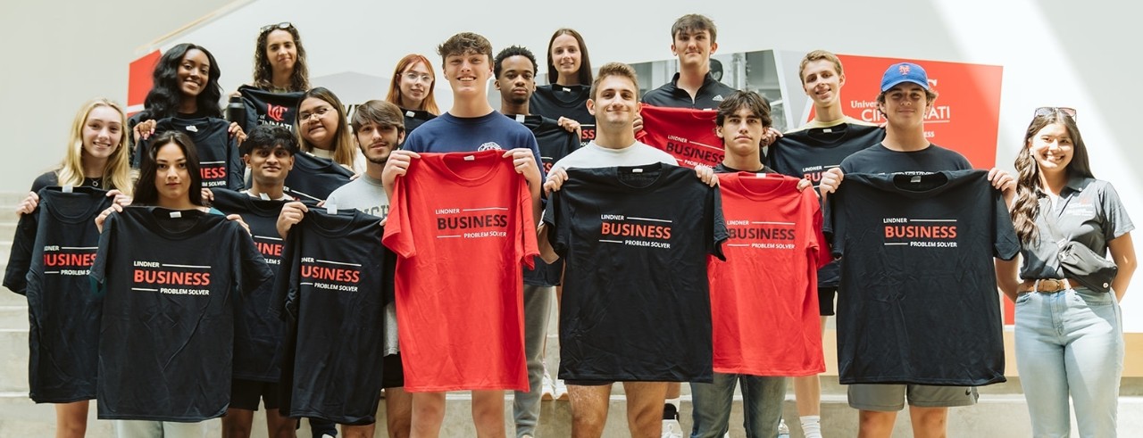 Students hold black and red Lindner-branded t-shirts while standings on the atrium steps.