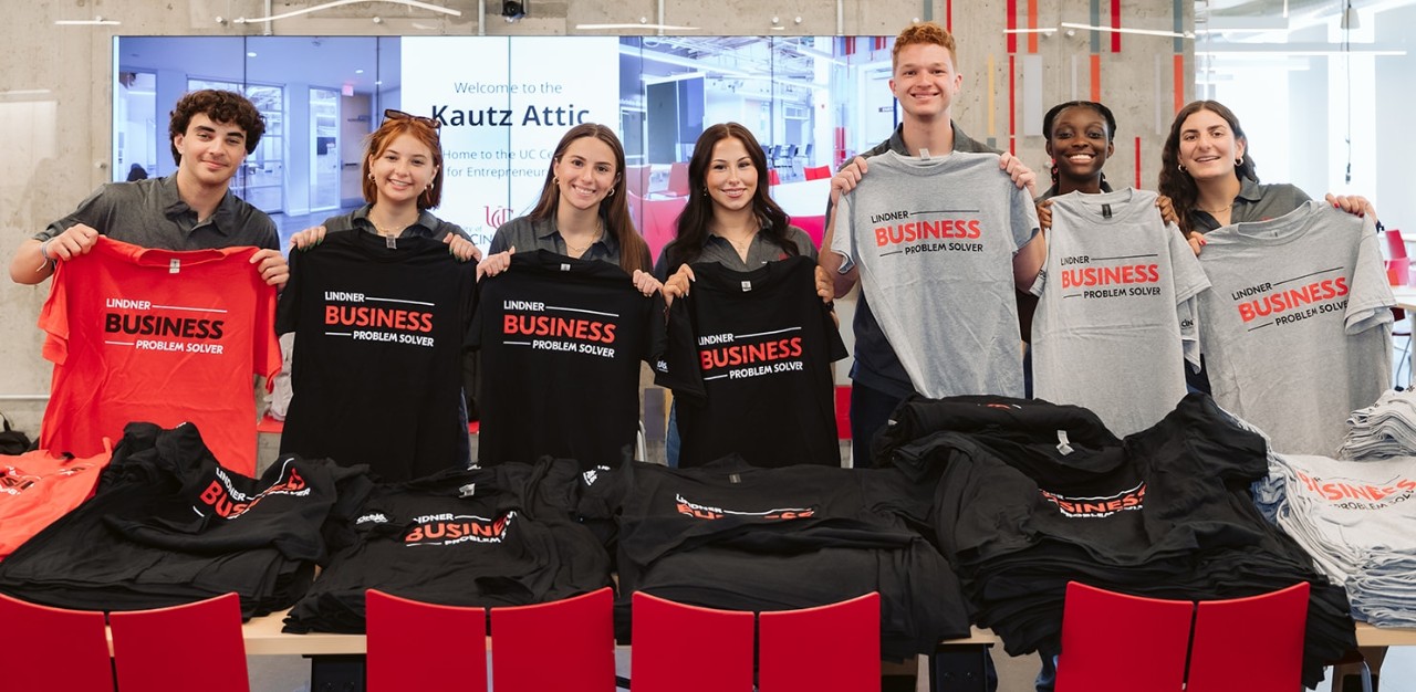 Students hold black, red and gray Lindner-branded t-shirts in a classroom.